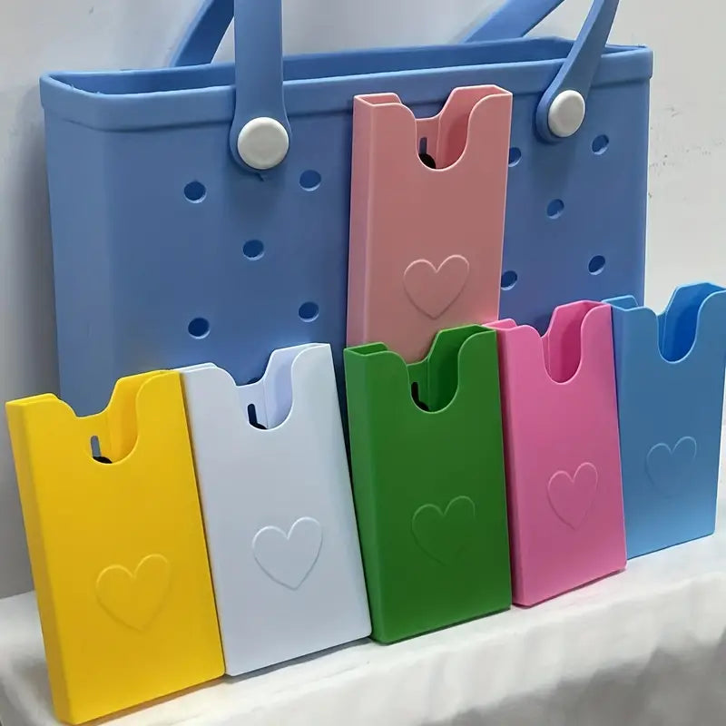 A collection of Bog Bag Phone Holders in various colors including blue, pink, green, white, and yellow, all featuring a heart shape on the front.
