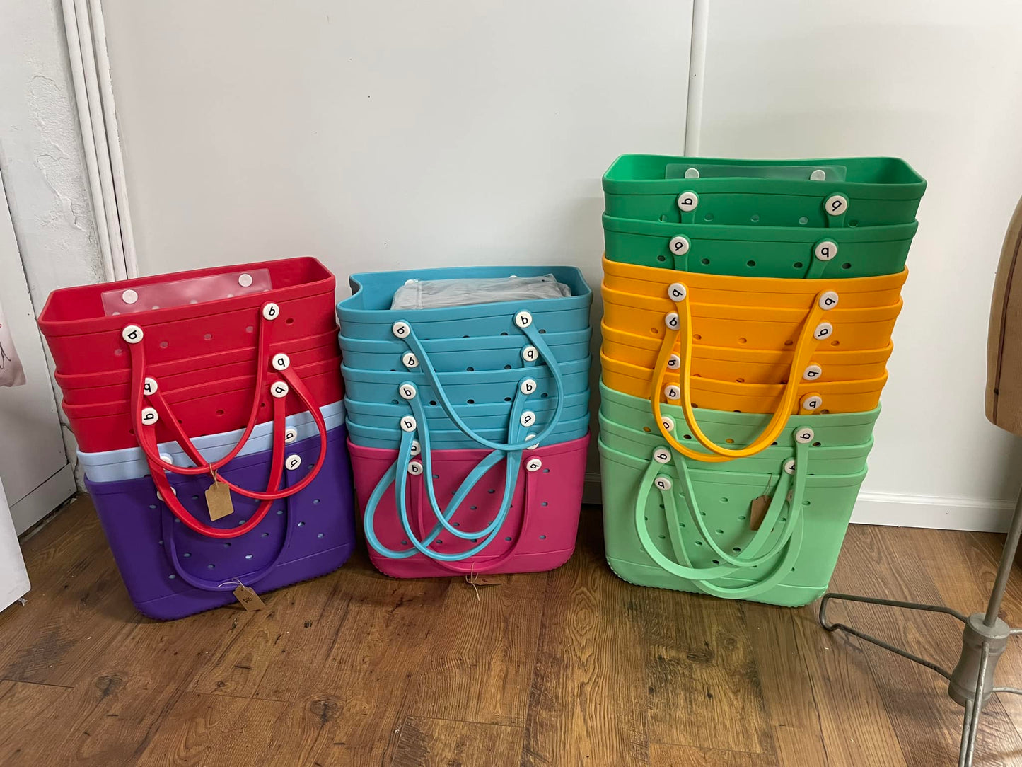 A set of colorful fabric bags standing upright on the floor. They appear to be empty and have a simple solid color design with metallic hardware.
