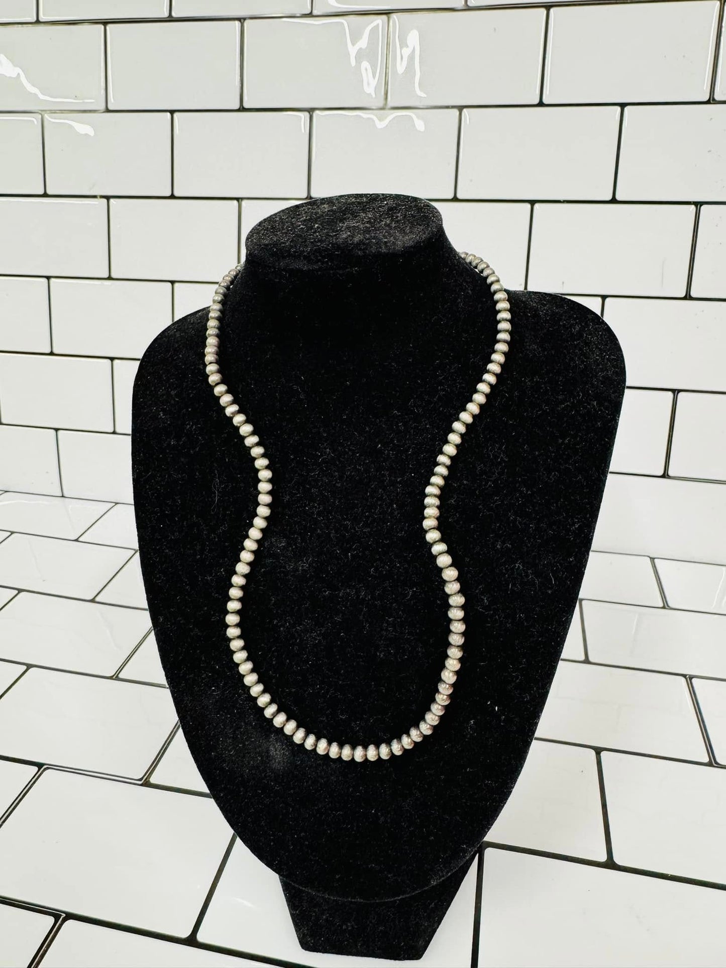 Faux Navajo Pearls Necklace – close-up – Silver-toned faux Navajo pearl necklace with oxidized finish.
Faux Navajo Pearls Bracelet – stacked view – Multiple faux Navajo pearl bracelets layered together.
Faux Navajo Pearls Necklace – full view – Long beaded faux Navajo pearl necklace displayed on flat background.
Lifestyle image – faux pearls worn – Model wearing faux Navajo pearls necklace and bracelet set.
Faux Navajo Pearls jewelry – mix and match display – Multiple lengths and bracelet sizes shown togeth