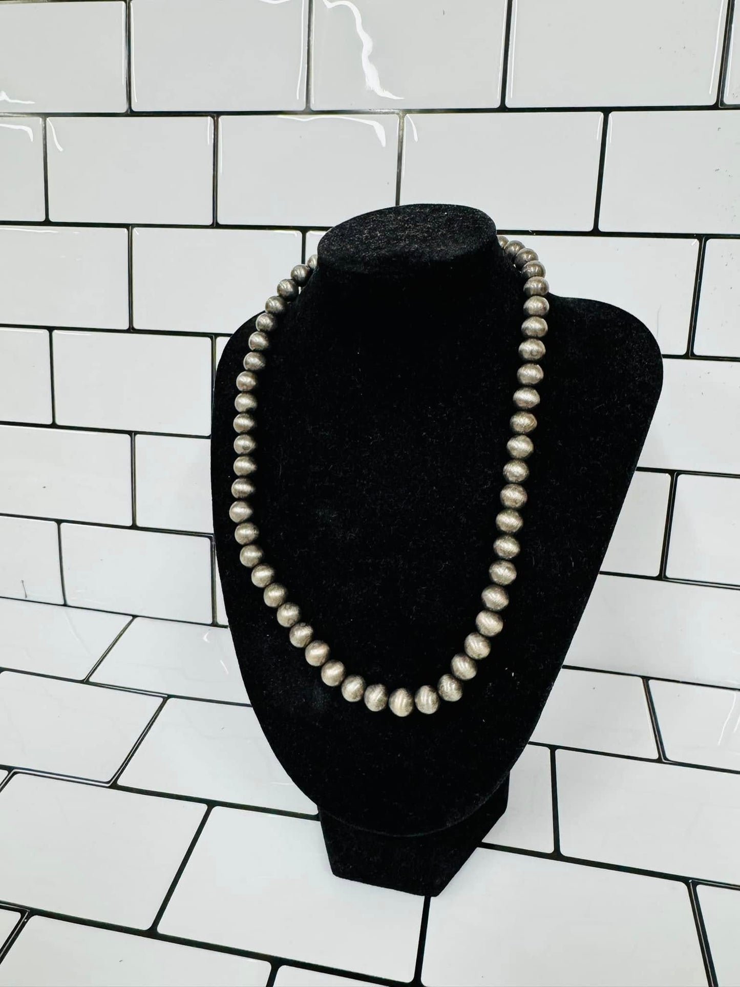 A necklace displayed on a mannequin bust with white pearl-like beads against a white tiled background.