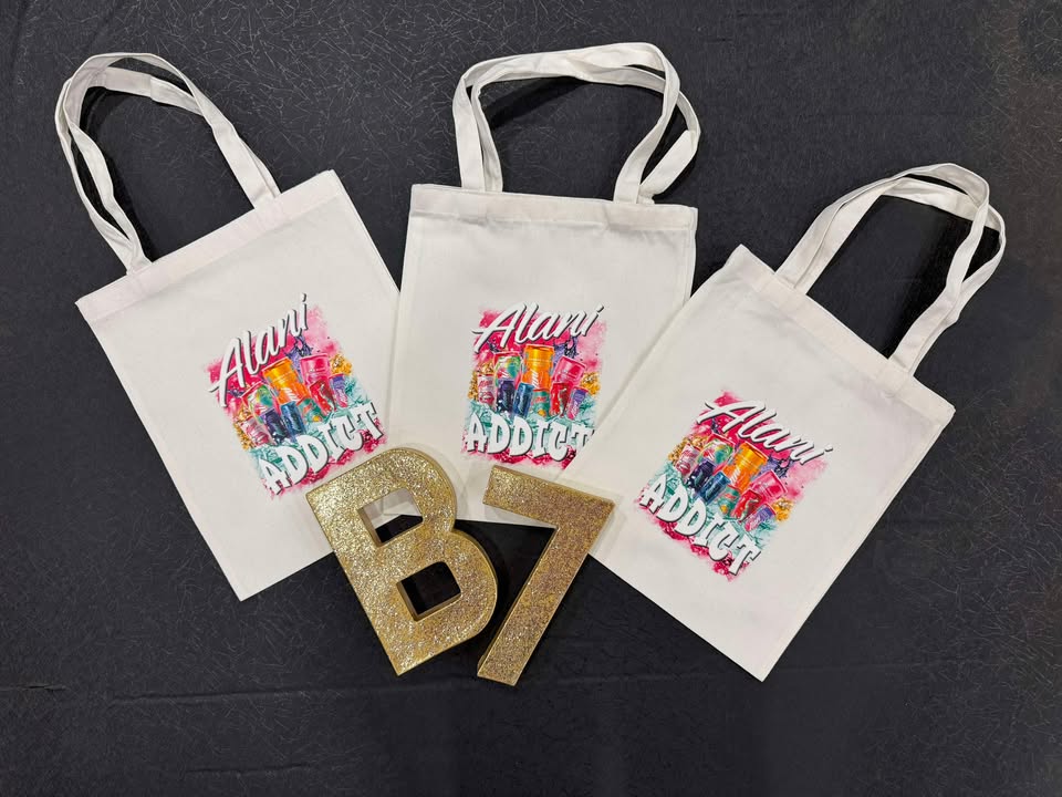 Three white tote bags with the Alani Addict logo printed in multicolor. The logo includes text and a stylized graphic element.