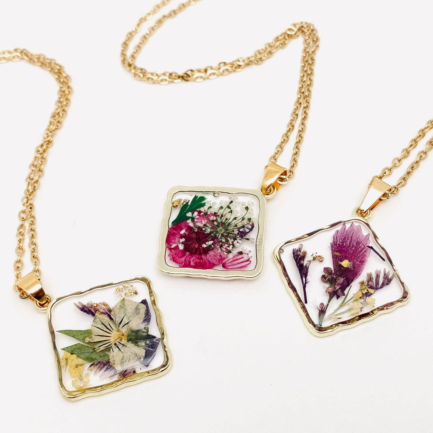 Square pendant necklace with pressed floral arrangement in resin
Close-up of dried flowers encased in clear resin square frame
Necklace styled over neutral top showing copper frame & stainless steel chain