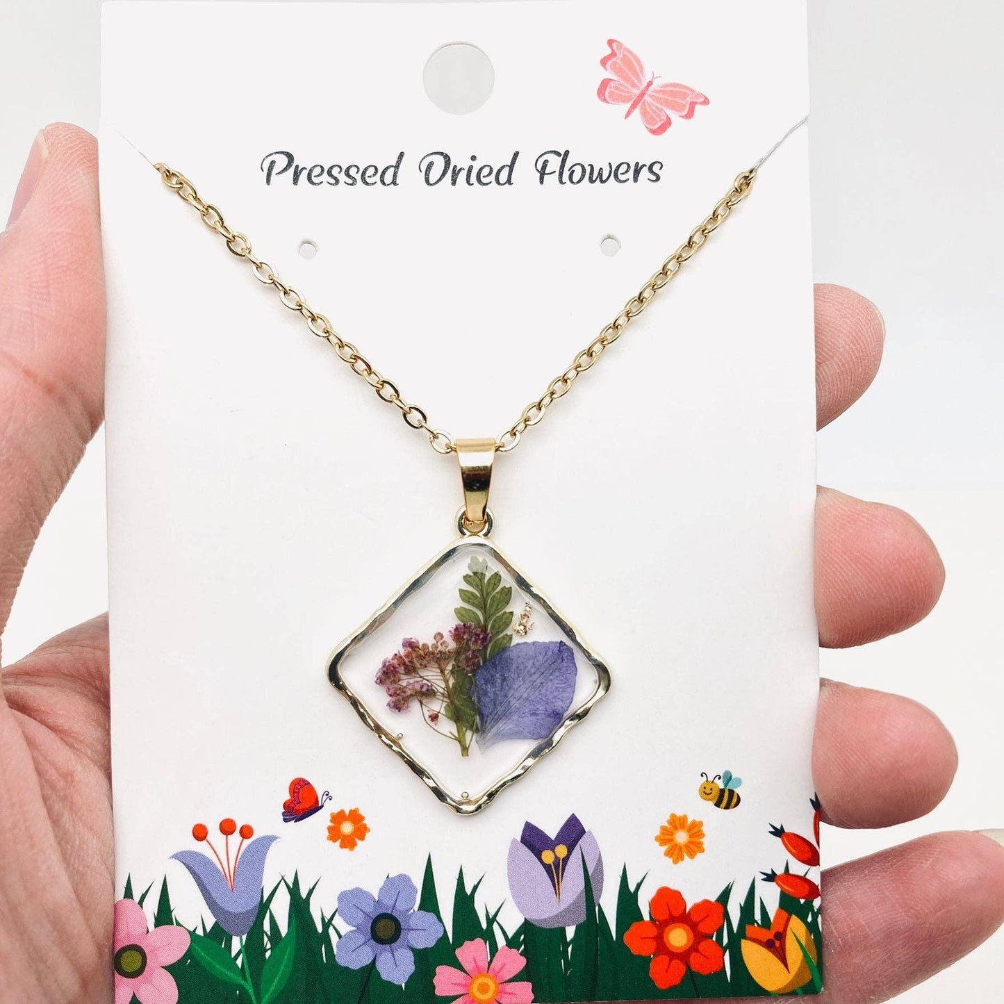Square pendant necklace with pressed floral arrangement in resin
Close-up of dried flowers encased in clear resin square frame
Necklace styled over neutral top showing copper frame & stainless steel chain