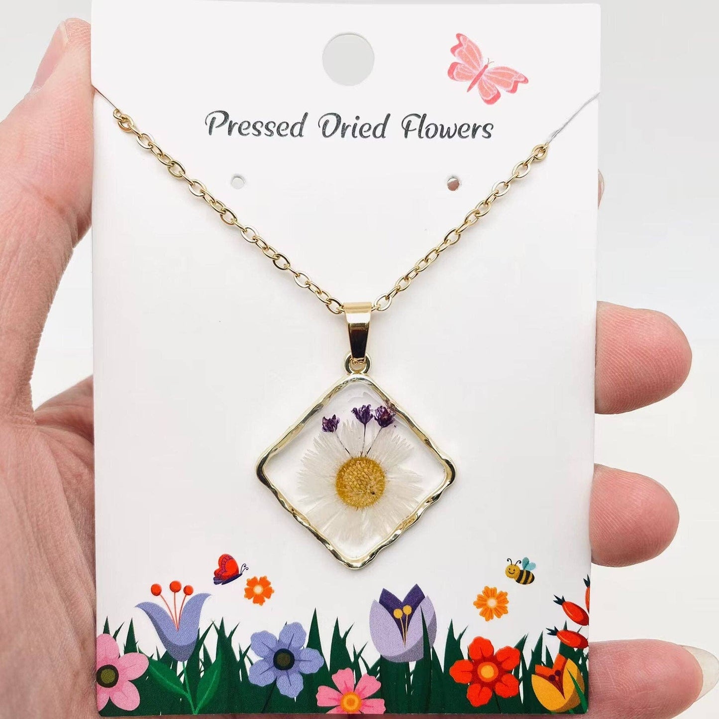 Square pendant necklace with pressed floral arrangement in resin
Close-up of dried flowers encased in clear resin square frame
Necklace styled over neutral top showing copper frame & stainless steel chain