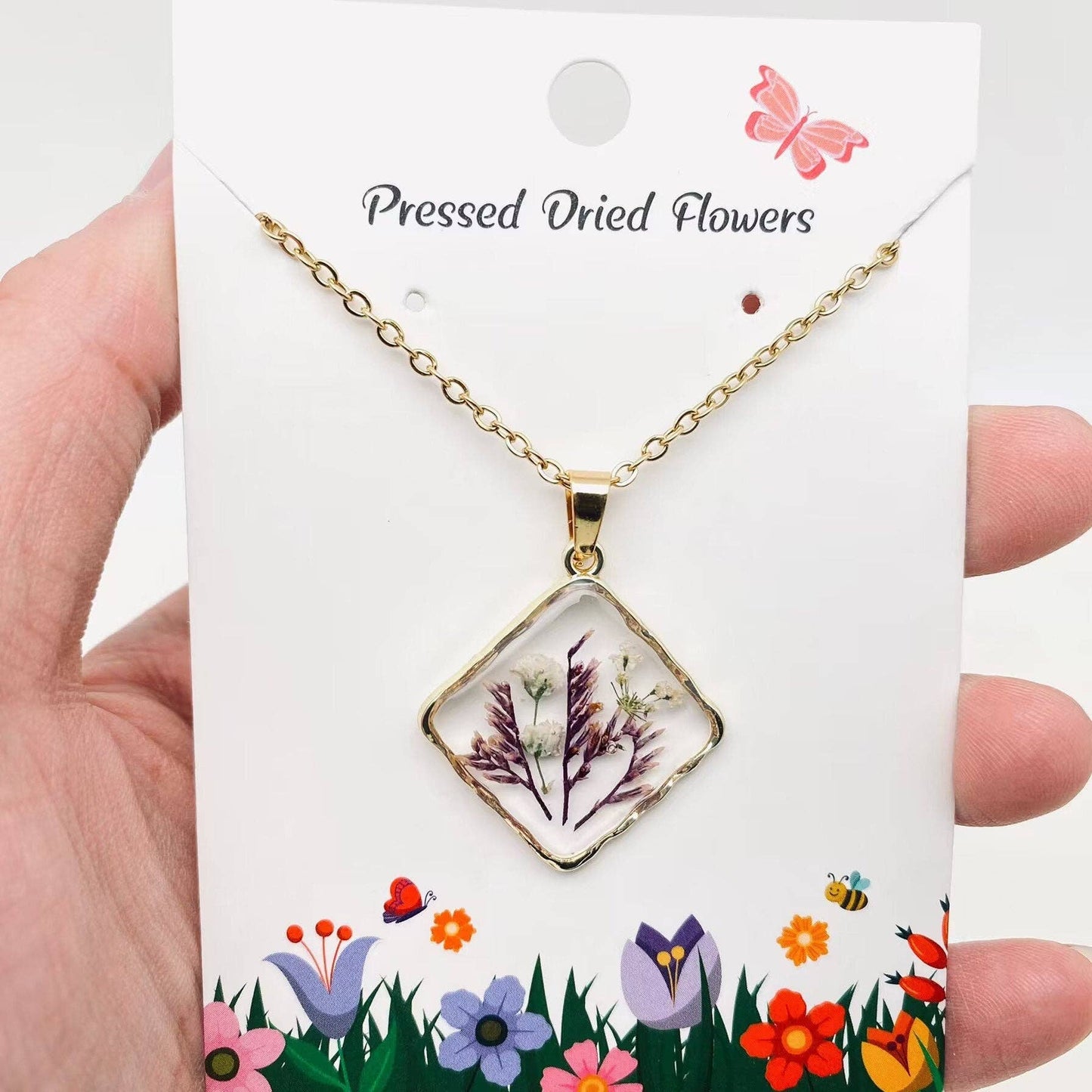 Square pendant necklace with pressed floral arrangement in resin
Close-up of dried flowers encased in clear resin square frame
Necklace styled over neutral top showing copper frame & stainless steel chain