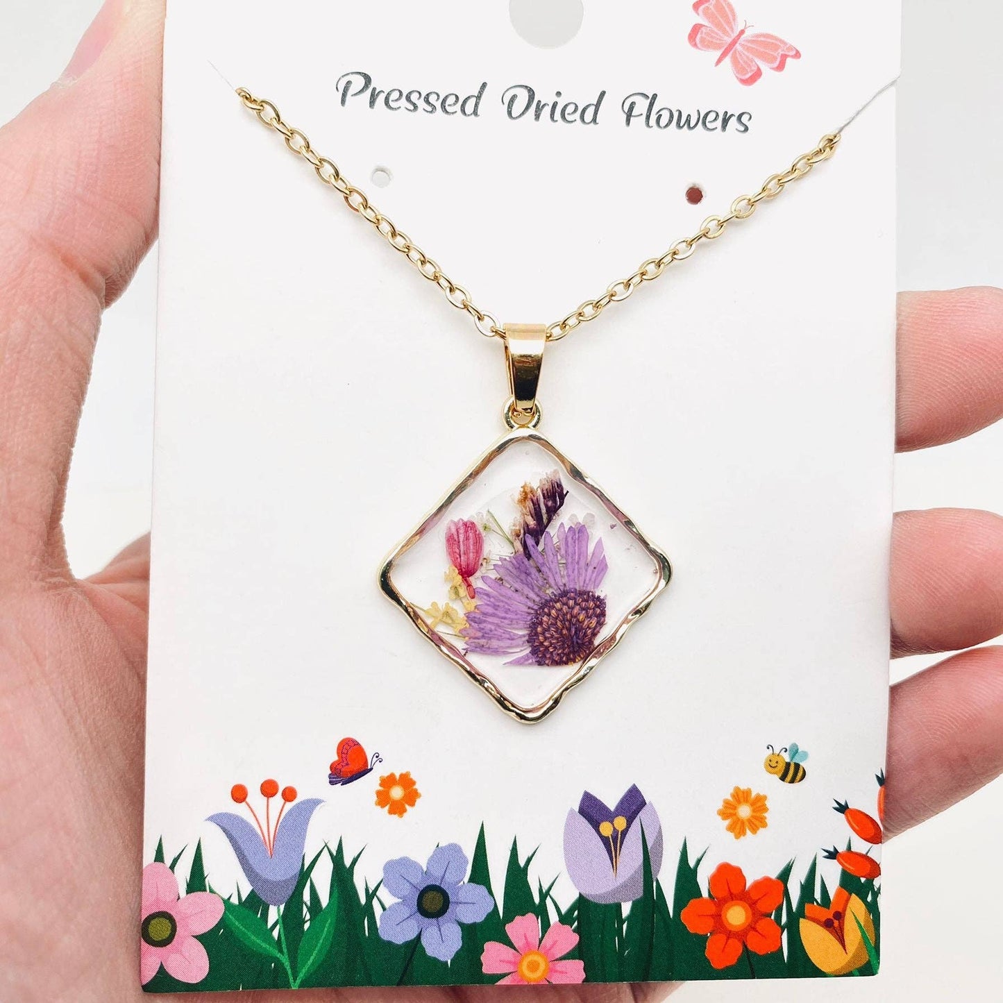 Square pendant necklace with pressed floral arrangement in resin
Close-up of dried flowers encased in clear resin square frame
Necklace styled over neutral top showing copper frame & stainless steel chain