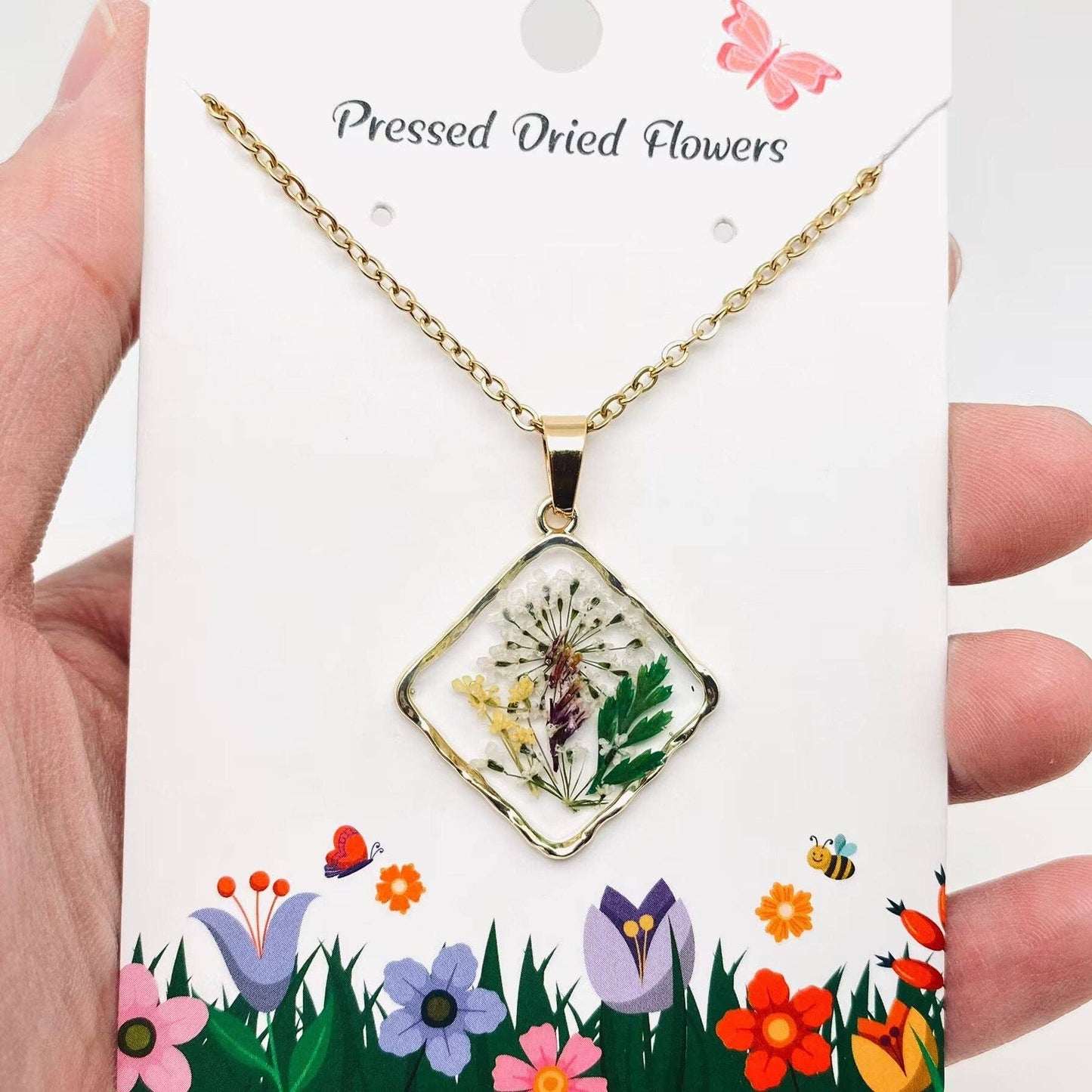 Square pendant necklace with pressed floral arrangement in resin
Close-up of dried flowers encased in clear resin square frame
Necklace styled over neutral top showing copper frame & stainless steel chain