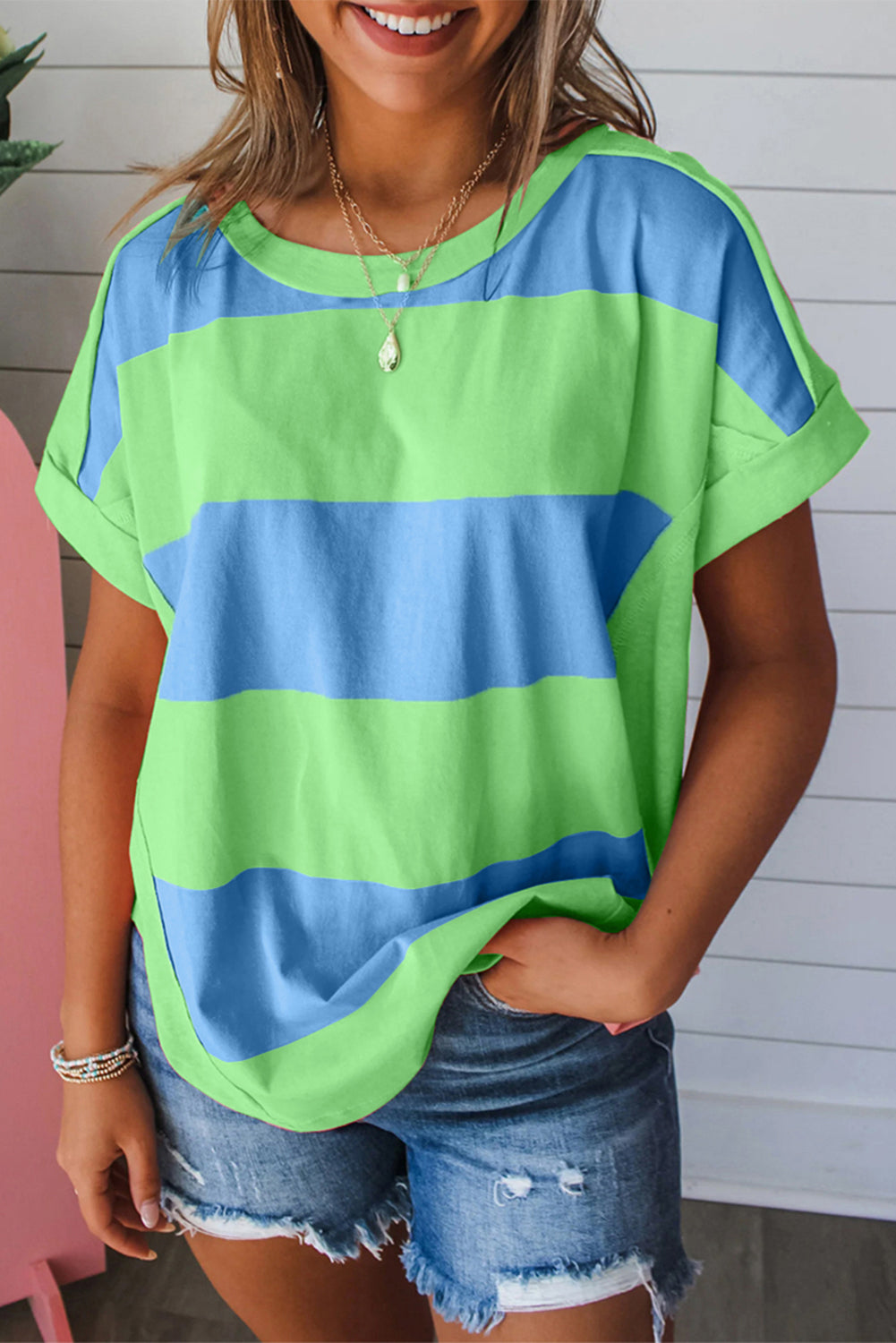 A woman wearing a blue and green colorblock loose t-shirt with a rounded hem, paired with denim shorts.