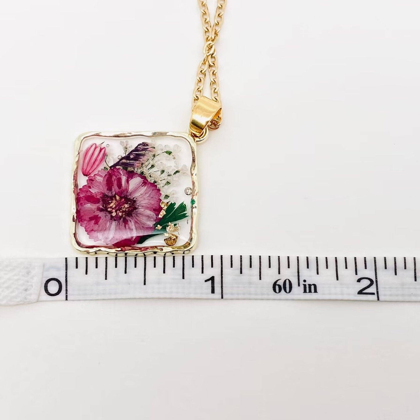 Square pendant necklace with pressed floral arrangement in resin
Close-up of dried flowers encased in clear resin square frame
Necklace styled over neutral top showing copper frame & stainless steel chain