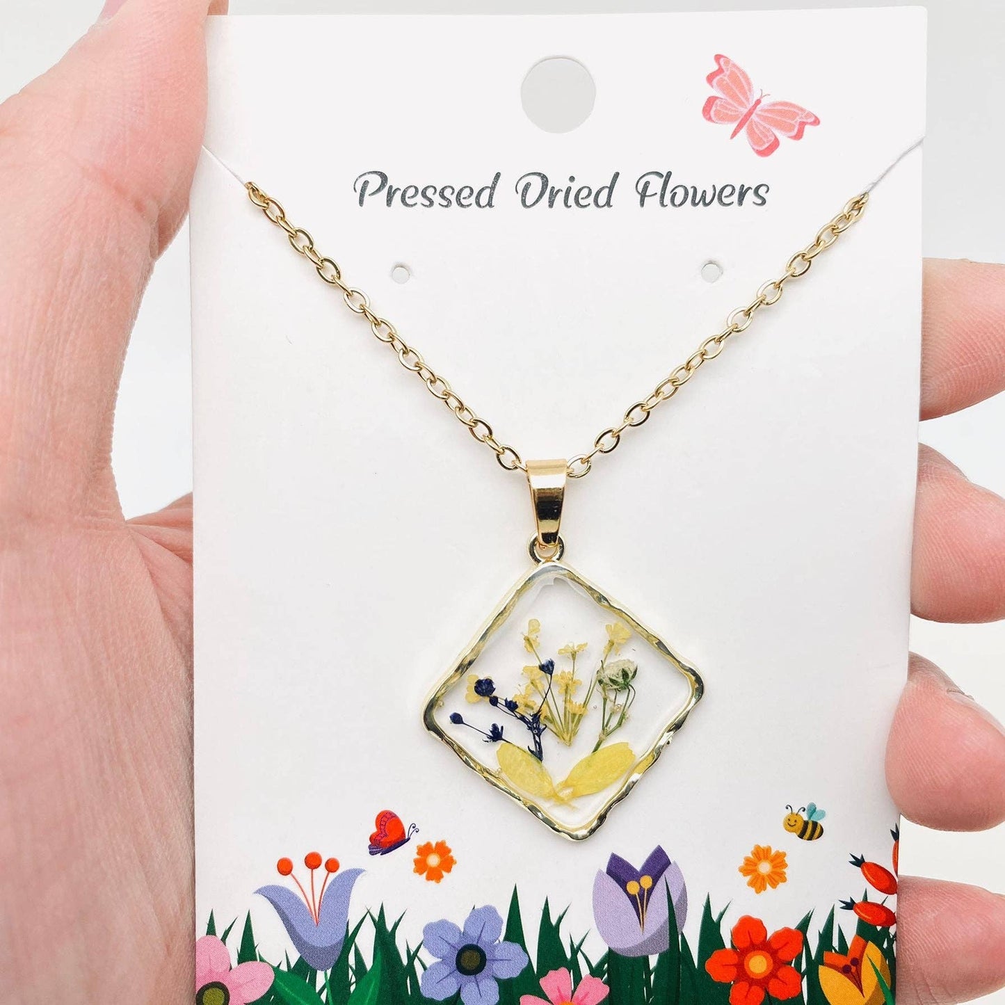 Square pendant necklace with pressed floral arrangement in resin
Close-up of dried flowers encased in clear resin square frame
Necklace styled over neutral top showing copper frame & stainless steel chain