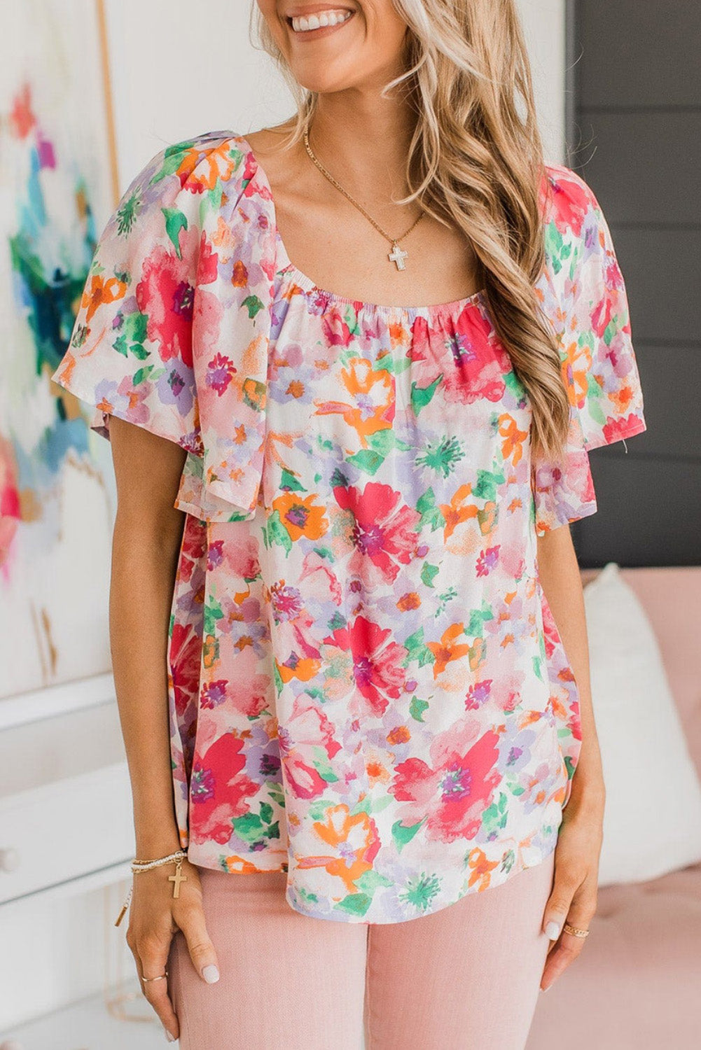 A woman wearing a multicolor watercolor floral square neck ruffle sleeve blouse with short sleeves.