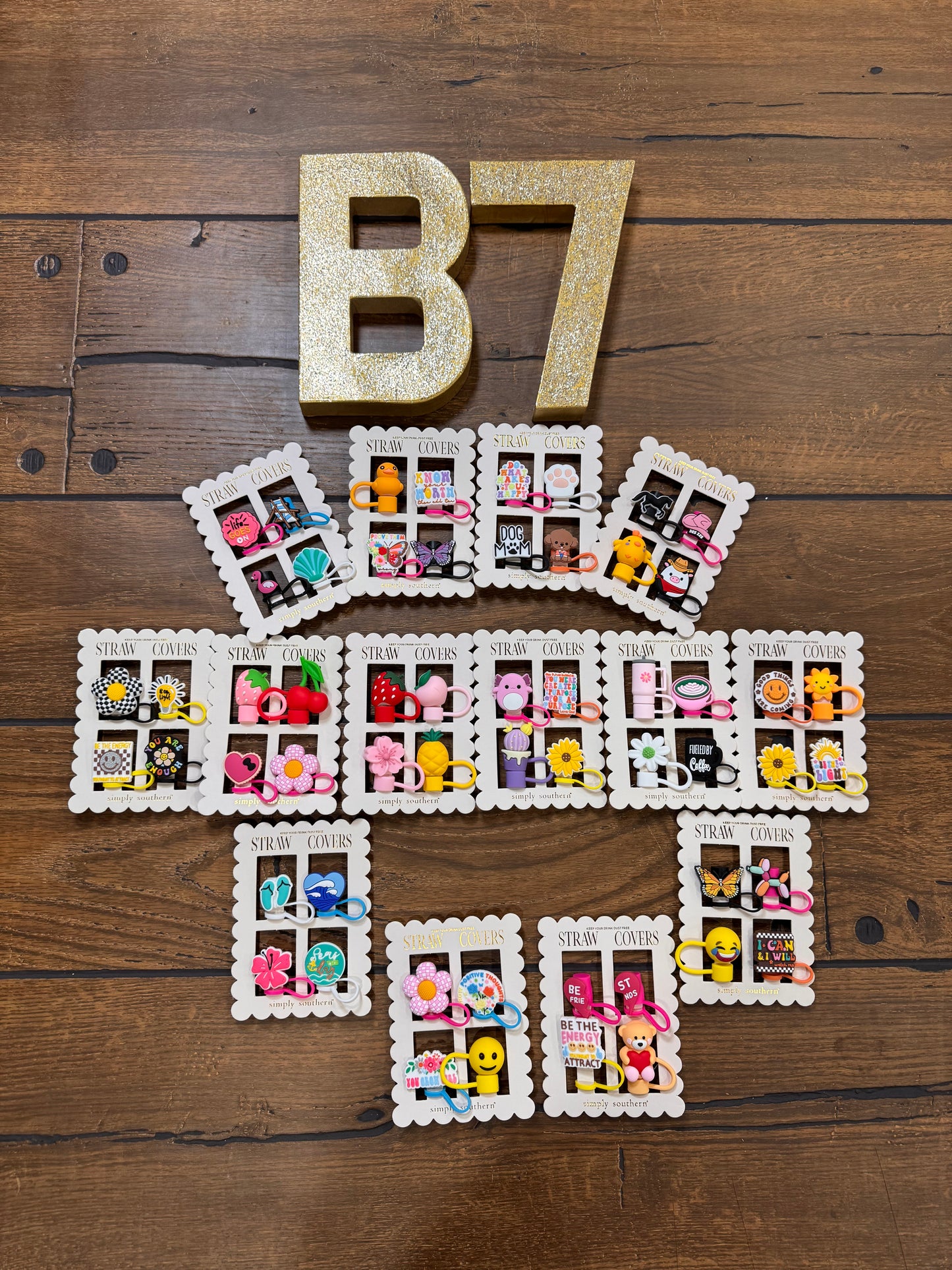 A collection of Simply Southern Strawberry Covers displayed on a wooden surface, with each cover featuring a different strawberry design. The letter 'B7' is also present in gold lettering at the top.