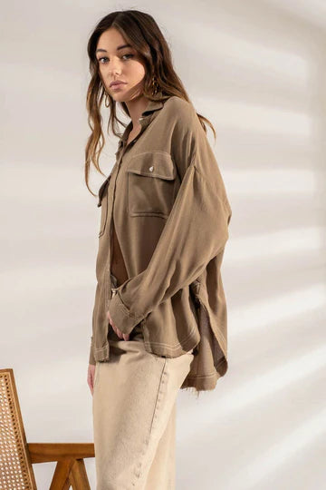 Olive oversized button-down shacket with frayed hem laid flat
Close-up of contrast stitching and chest pocket tab detail
View of raw hem edge and drape of oversized silhouette