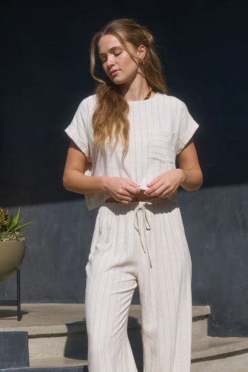A woman wearing a beige pinstripe crop top with short cuff sleeves and a back button design.