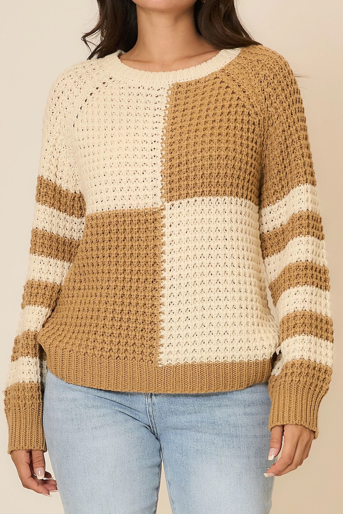 Person wearing a brown and beige striped sweater with light blue jeans on a beige background