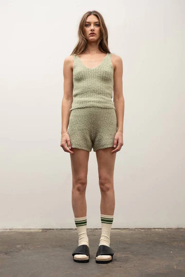 A woman standing, wearing a green scoop neck, sleeveless tank top with a fuzzy texture, and matching shorts.