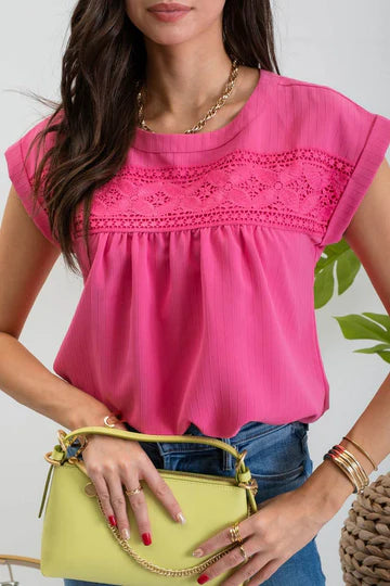 A model wearing a pink top with floral eyelet lace trim and back button detail.