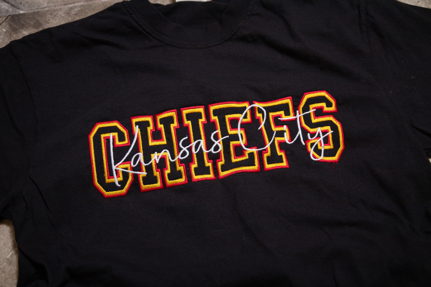 Black t-shirt with 'Kansas City Chiefs' text in colorful letters on a dark background