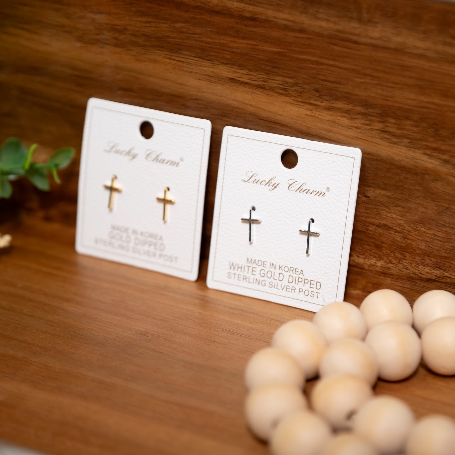 Two pairs of cross-shaped earrings on 'Lucky Charm' cards with wooden beads in the foreground.