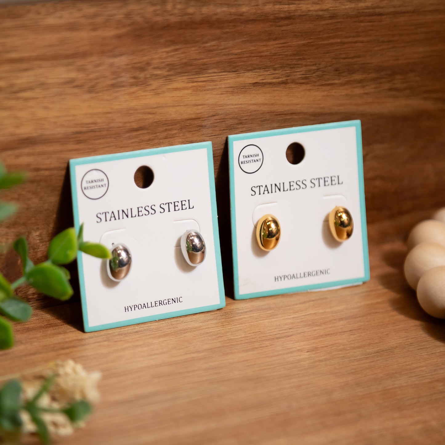 Two pairs of stainless steel earrings on display cards with a wooden background.