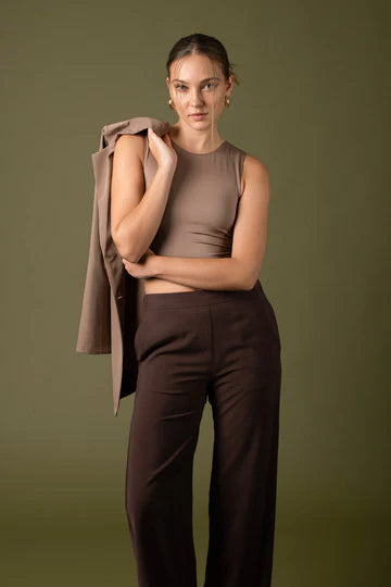 A model wearing a reversible knit cropped tank top with one side in solid blue and the other in a pepper pattern, paired with brown trousers.