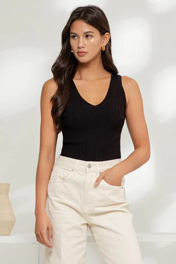 A woman wearing a sleeveless black v-neck sweater knit top with a keyhole back, paired with beige pants.