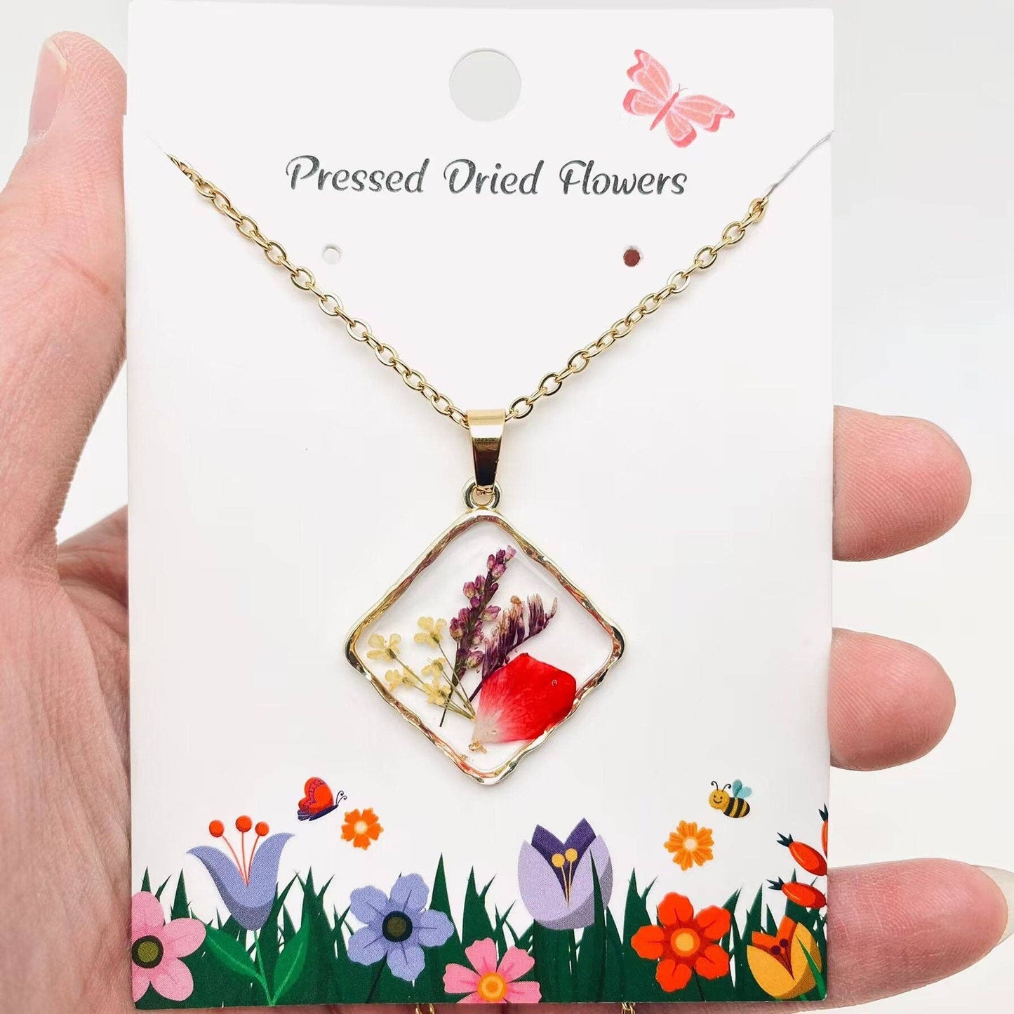 Square pendant necklace with pressed floral arrangement in resin
Close-up of dried flowers encased in clear resin square frame
Necklace styled over neutral top showing copper frame & stainless steel chain