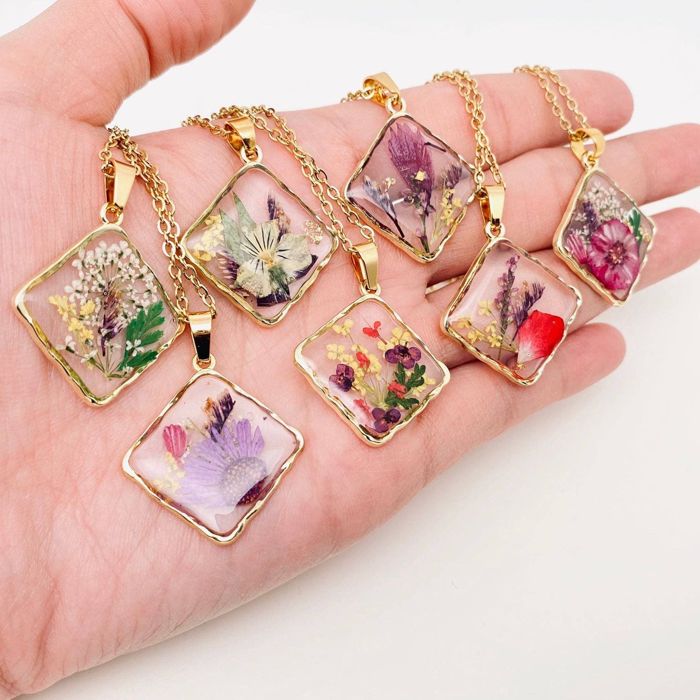 Square pendant necklace with pressed floral arrangement in resin
Close-up of dried flowers encased in clear resin square frame
Necklace styled over neutral top showing copper frame & stainless steel chain