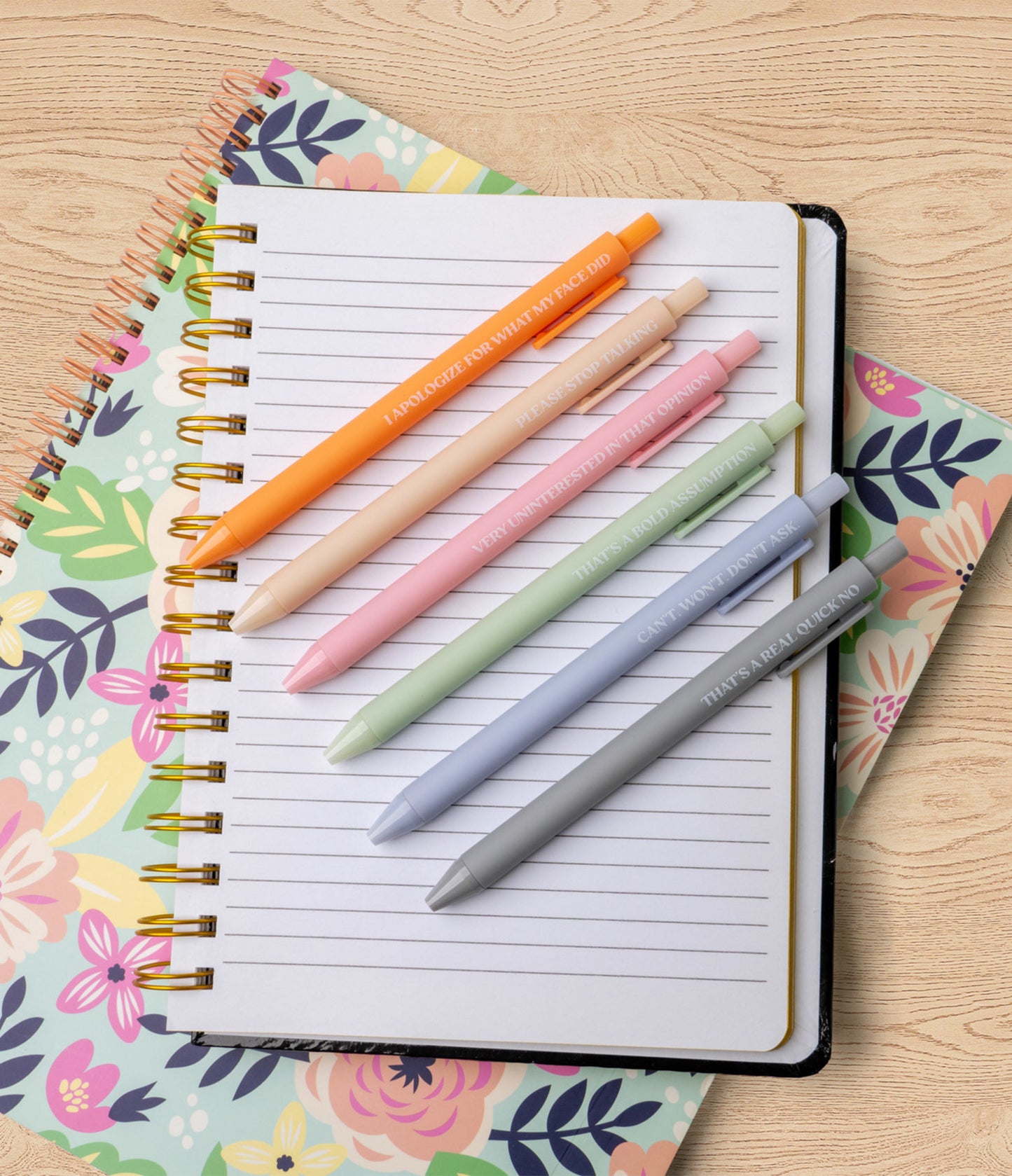 Colorful pens on a notebook with floral cover on a wooden surface