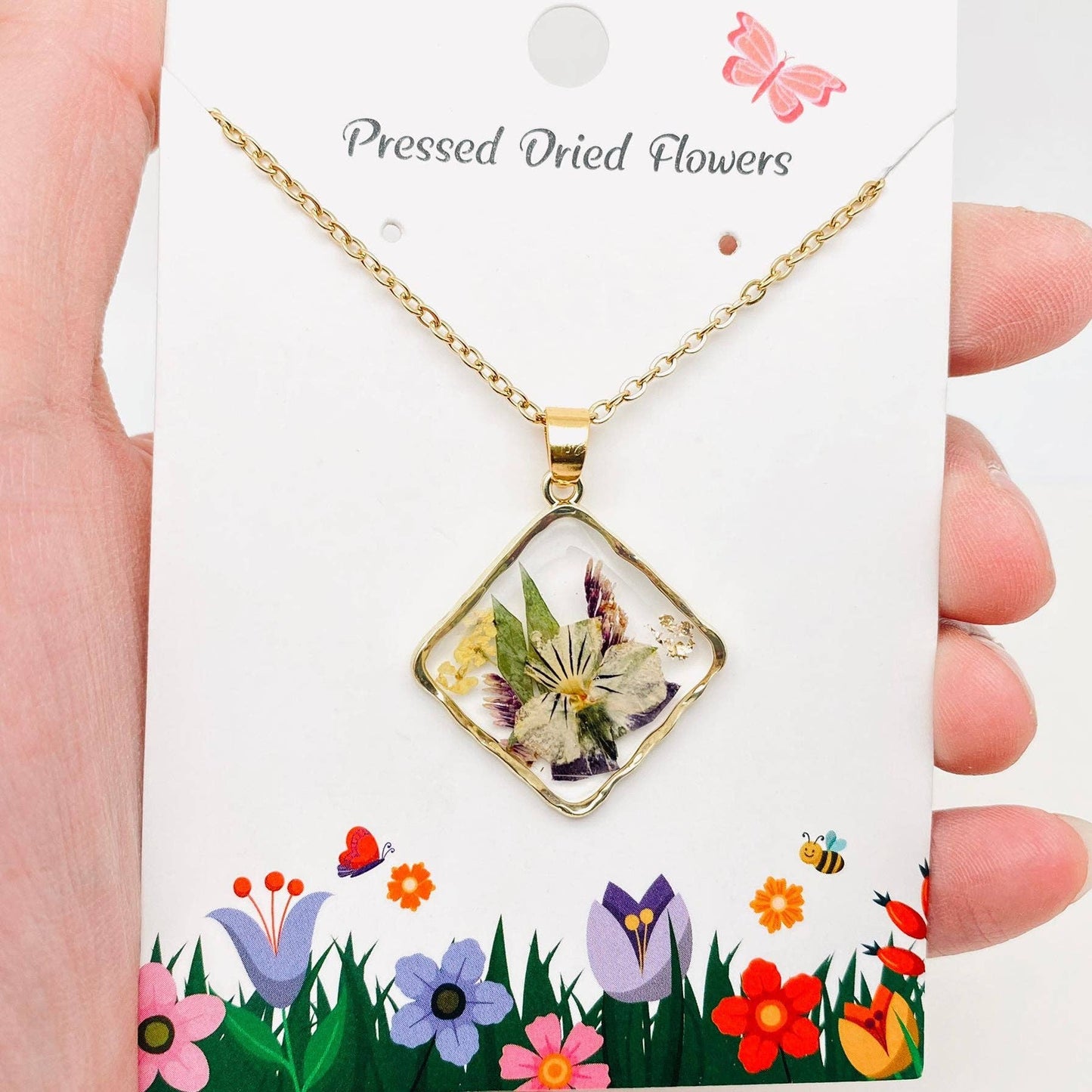 Square pendant necklace with pressed floral arrangement in resin
Close-up of dried flowers encased in clear resin square frame
Necklace styled over neutral top showing copper frame & stainless steel chain