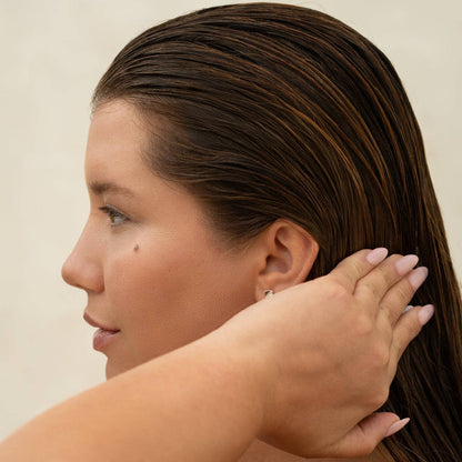 Woman with wet hair touching her ear against a neutral background