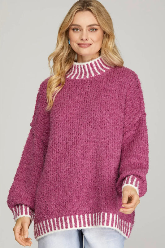 Woman wearing a pink knitted sweater with white trim on a gray background