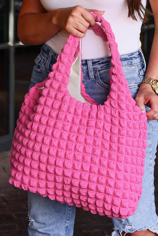 A person holding a rose red, puffy textured shopping bag with bubble pleats.