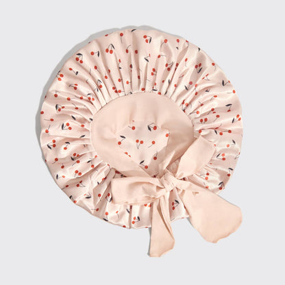 Beige shower cap with cherry pattern on a light gray background