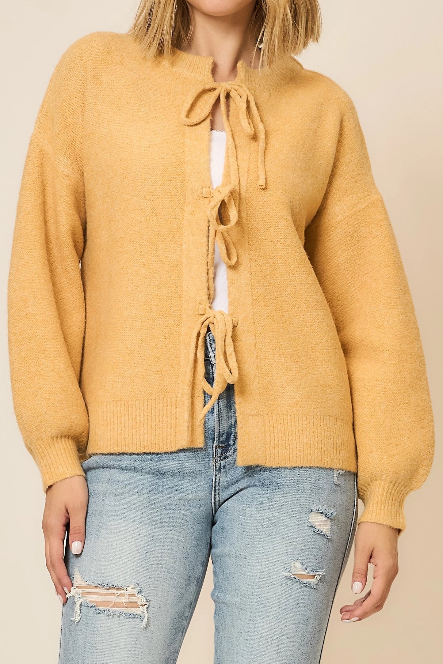 Mustard yellow cardigan with tie details worn by a person on a beige background
