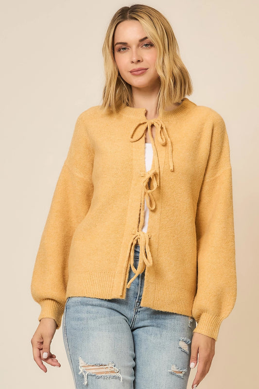 Woman wearing a mustard yellow cardigan with a tie front on a beige background