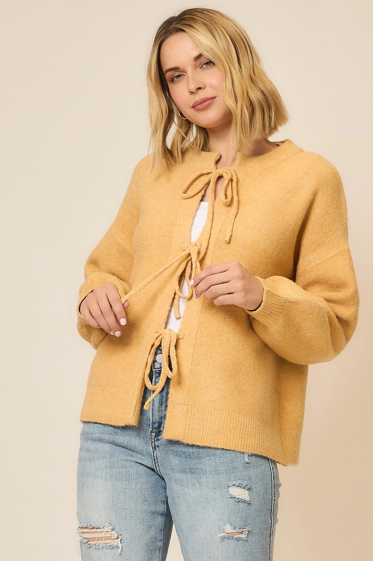 Woman wearing a mustard yellow cardigan with a beige background