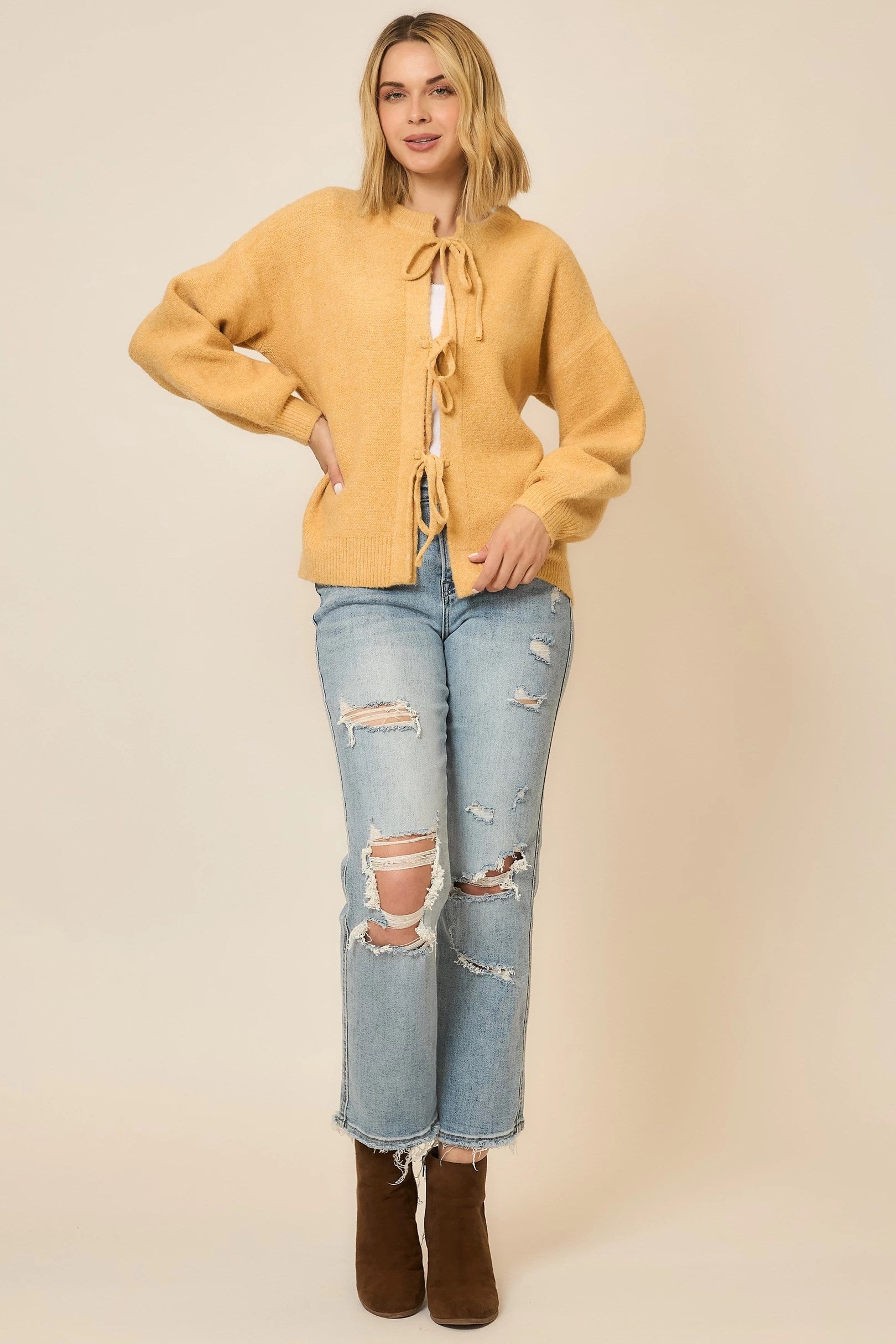 Woman wearing a mustard yellow cardigan, light blue jeans, and brown boots on a beige background