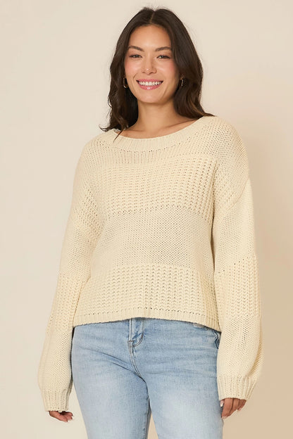 Woman wearing a light yellow sweater and blue jeans against a beige background