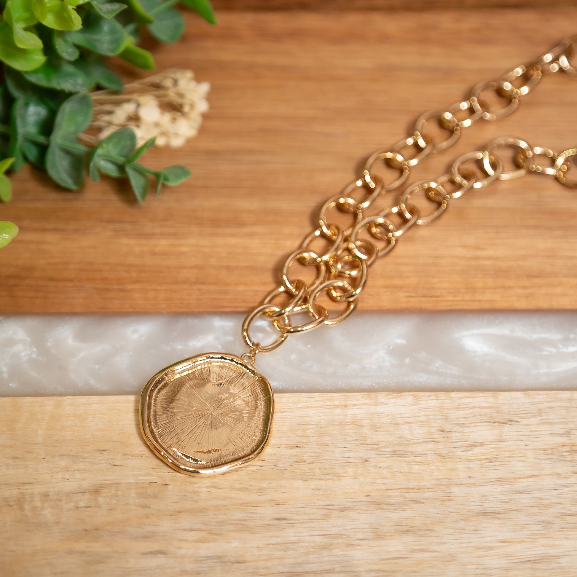Gold chain necklace with a round pendant on a wooden surface