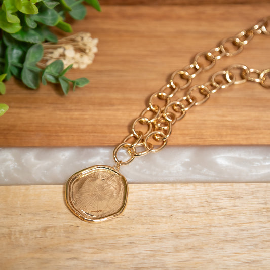 Gold chain necklace with a round pendant on a wooden surface