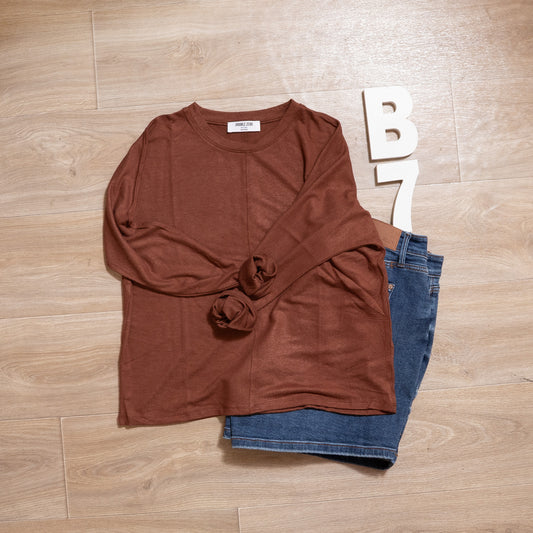 Brown long-sleeve shirt and blue jeans on a wooden floor with 'B7' letters.
