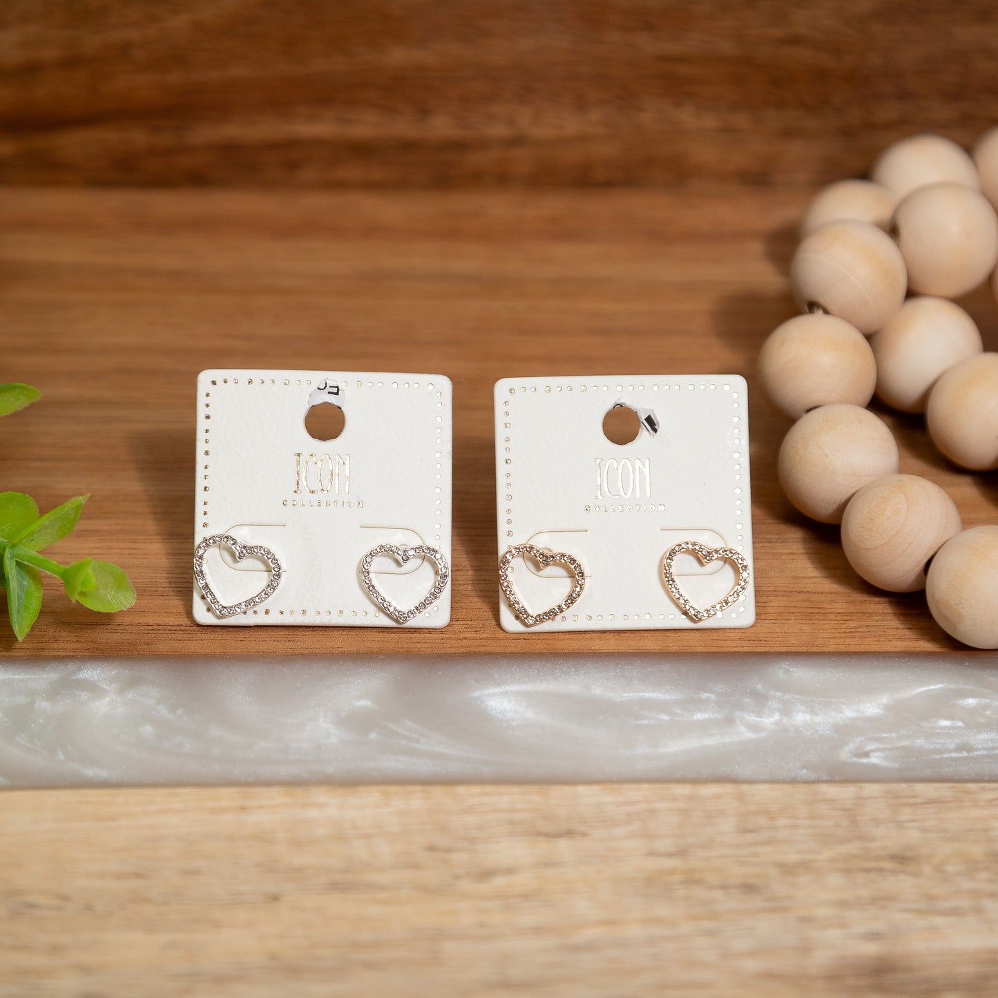Heart-shaped earrings on display cards with a wooden bead necklace and plant in the background.