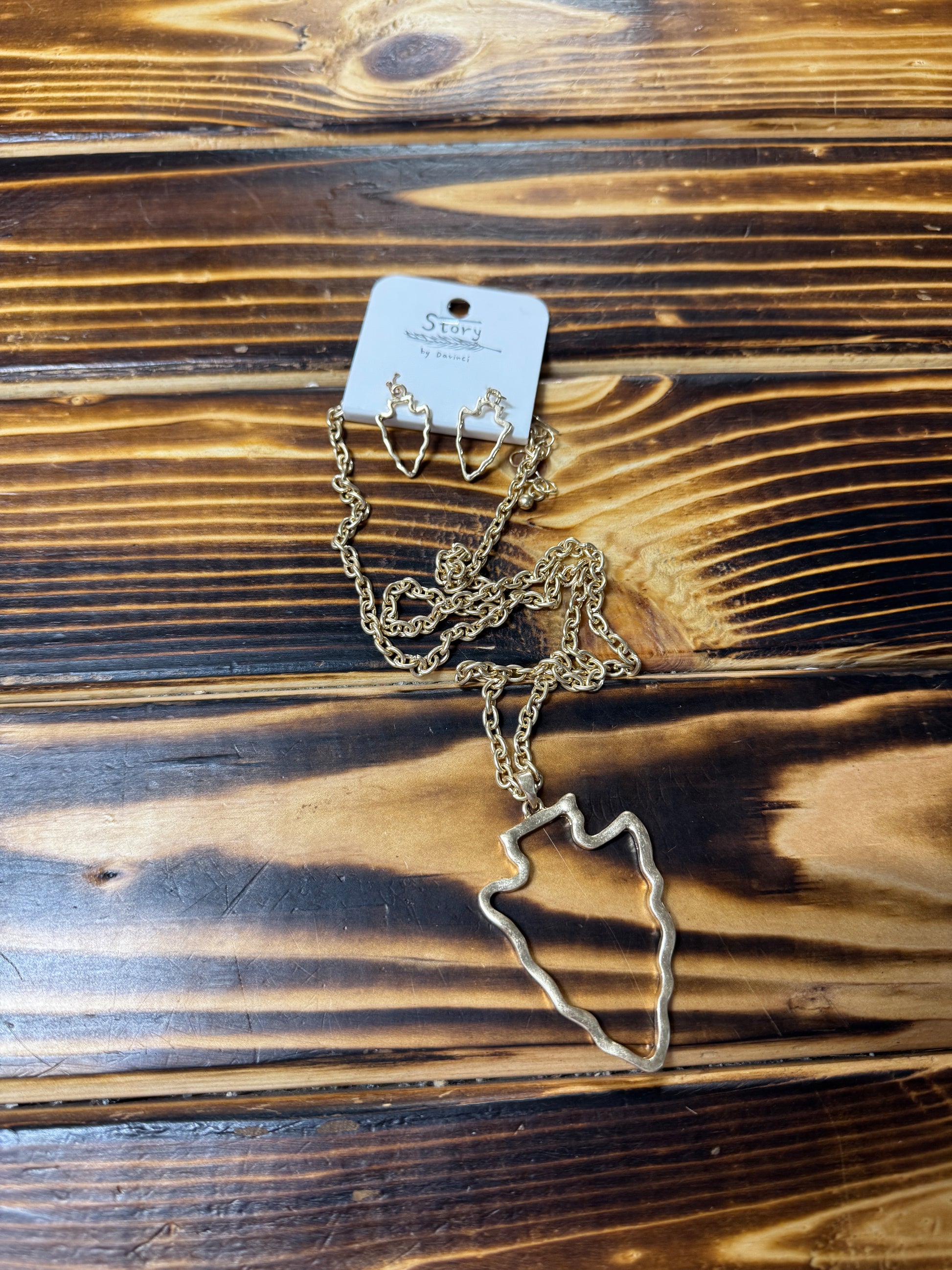 A hypoallergenic necklace and earring set with an arrow design, displayed on a wooden surface.