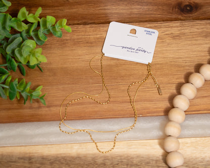 Gold necklace on a wooden surface with a 'garden party' card and a beaded bracelet.