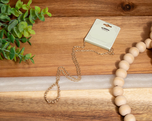 Gold necklace and wooden beads on a wooden surface with a plant in the corner