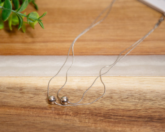 Silver necklace with two small round pendants on a wooden surface