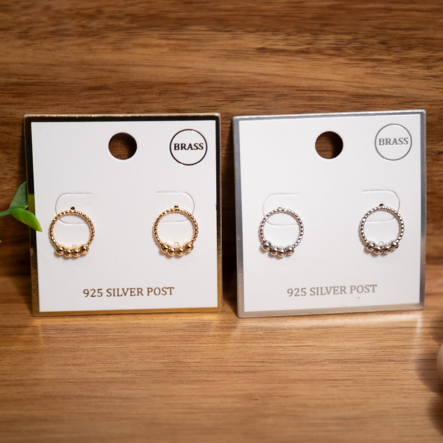 Two pairs of earrings on display cards with 'BRASS' and '925 SILVER POST' text on a wooden surface.