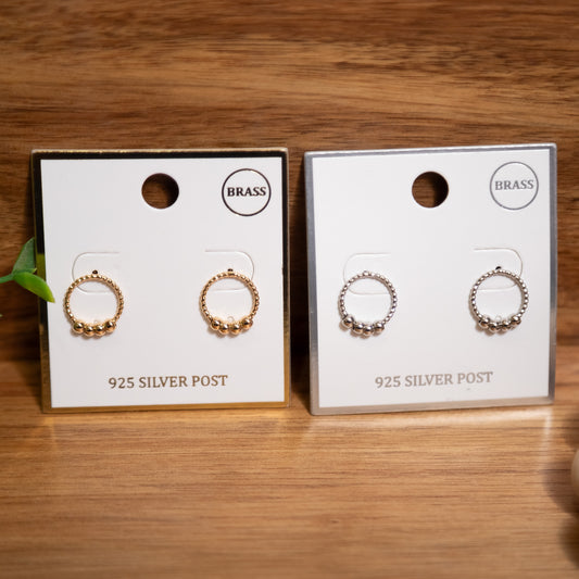 Two pairs of earrings on display cards with 'BRASS' and '925 SILVER POST' text on a wooden surface.