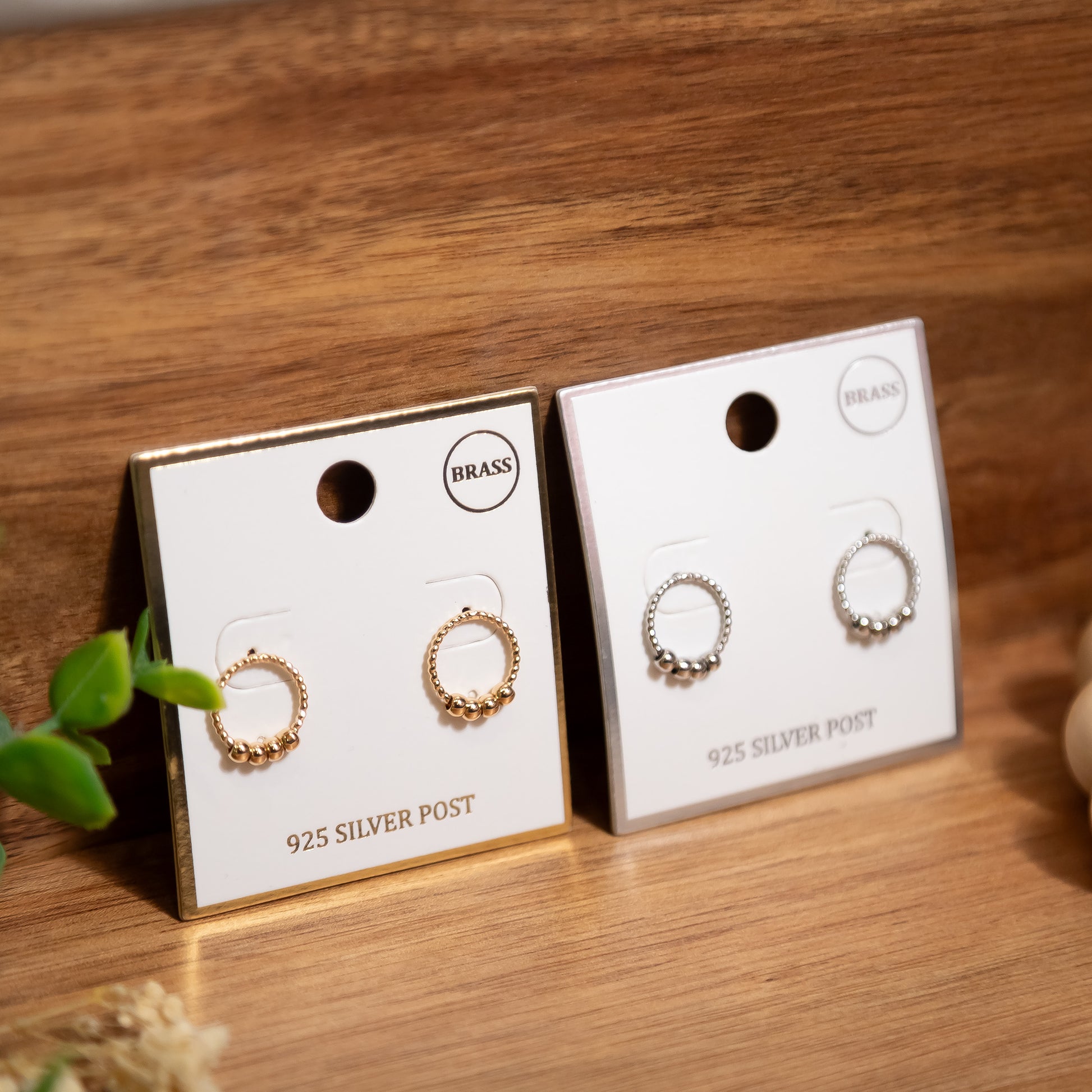 Two pairs of earrings on display cards with 'Brass' and 'Silver Post' labels on a wooden surface.
